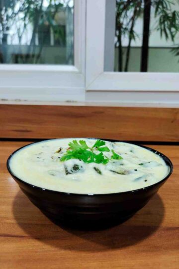 A bowl of Dahi Bhindi, a North Indian dish, showcasing tender okra in a tangy yogurt-based gravy, garnished with fresh coriander leaves, served warm or cold with roti, paratha, or rice. The dish is ready in 30 minutes, making it a perfect choice for a quick and satisfying weeknight dinner.