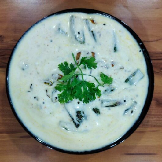 A bowl of Dahi Bhindi, a North Indian dish, showcasing tender okra in a tangy yogurt-based gravy, garnished with fresh coriander leaves, served warm or cold with roti, paratha, or rice. The dish is ready in 30 minutes, making it a perfect choice for a quick and satisfying weeknight dinner.