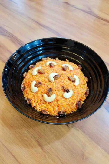 Delicious Gajar Halwa served in a bowl, garnished with golden-fried cashews and almonds. The vibrant orange color of the grated carrots cooked in milk and ghee creates a mouth-watering visual appeal.