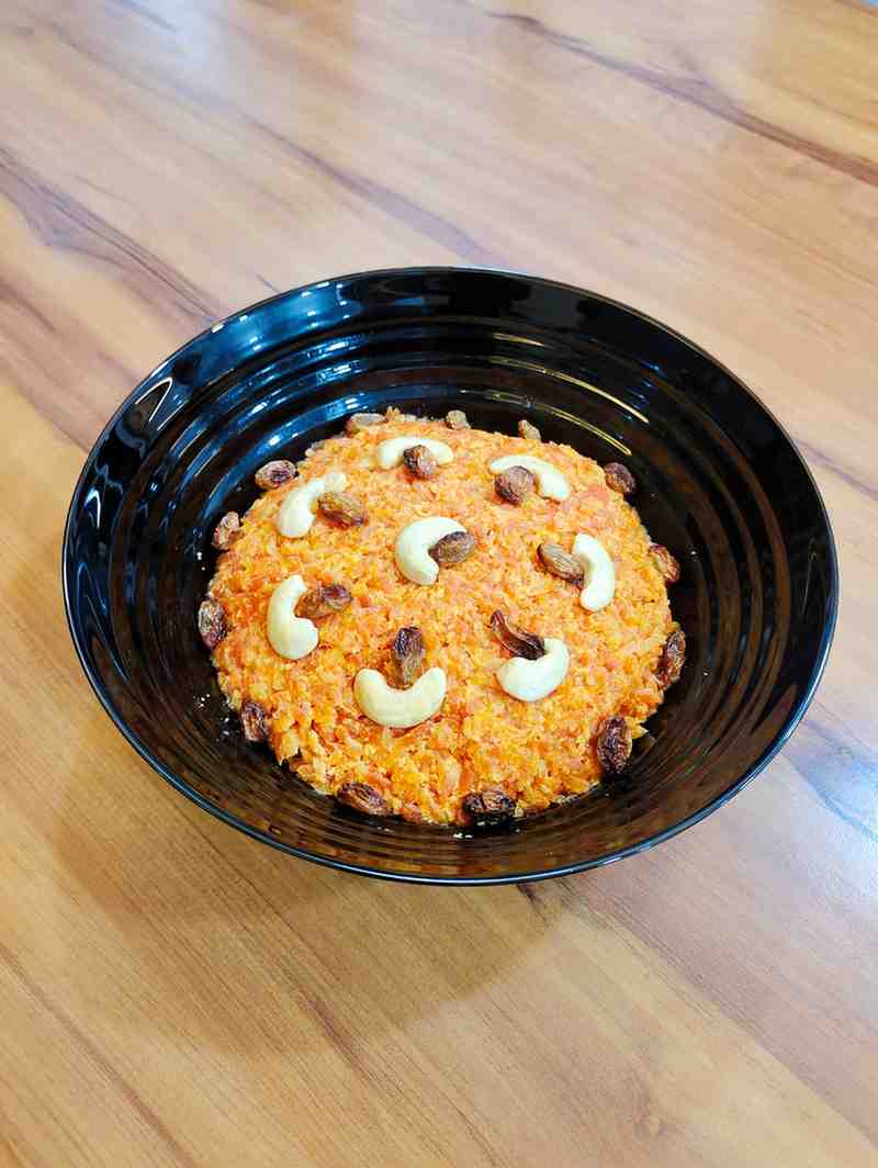 Delicious Gajar Halwa served in a bowl, garnished with golden-fried cashews and almonds. The vibrant orange color of the grated carrots cooked in milk and ghee creates a mouth-watering visual appeal.